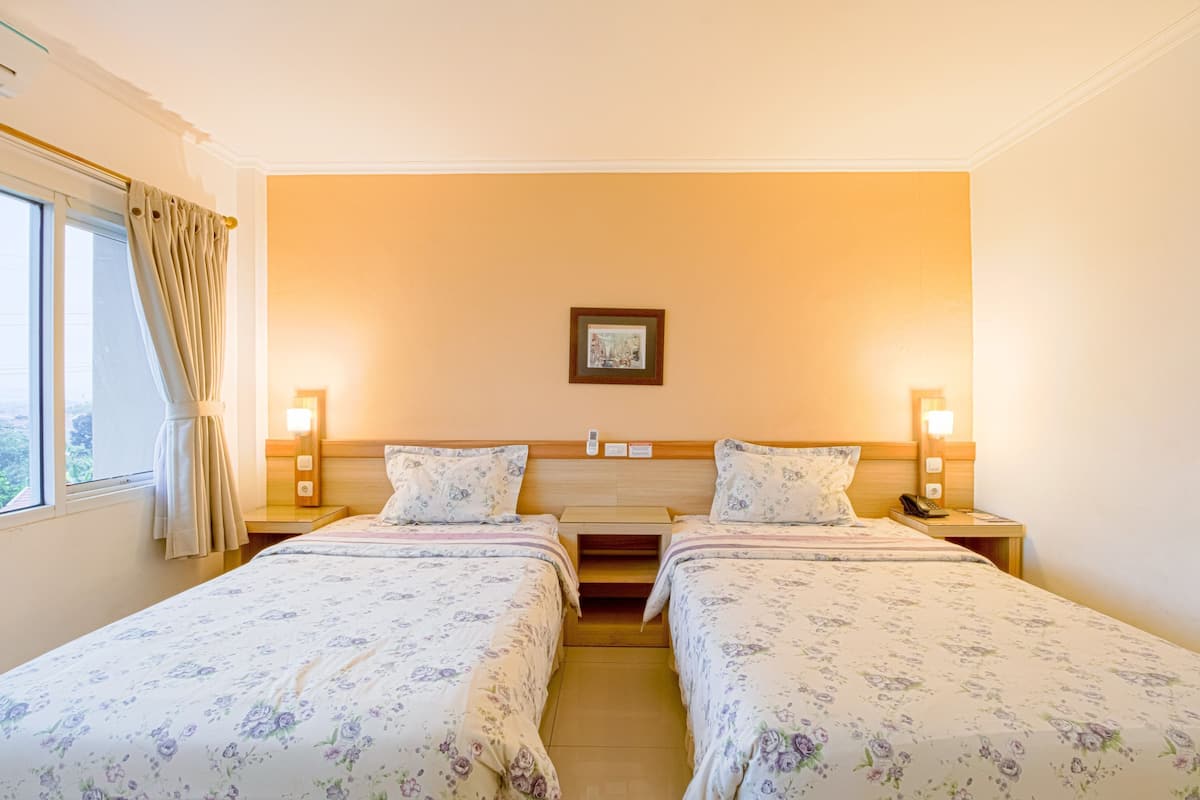A hotel room with two beds, a window with curtains, a framed picture on the wall, and bedside lamps.