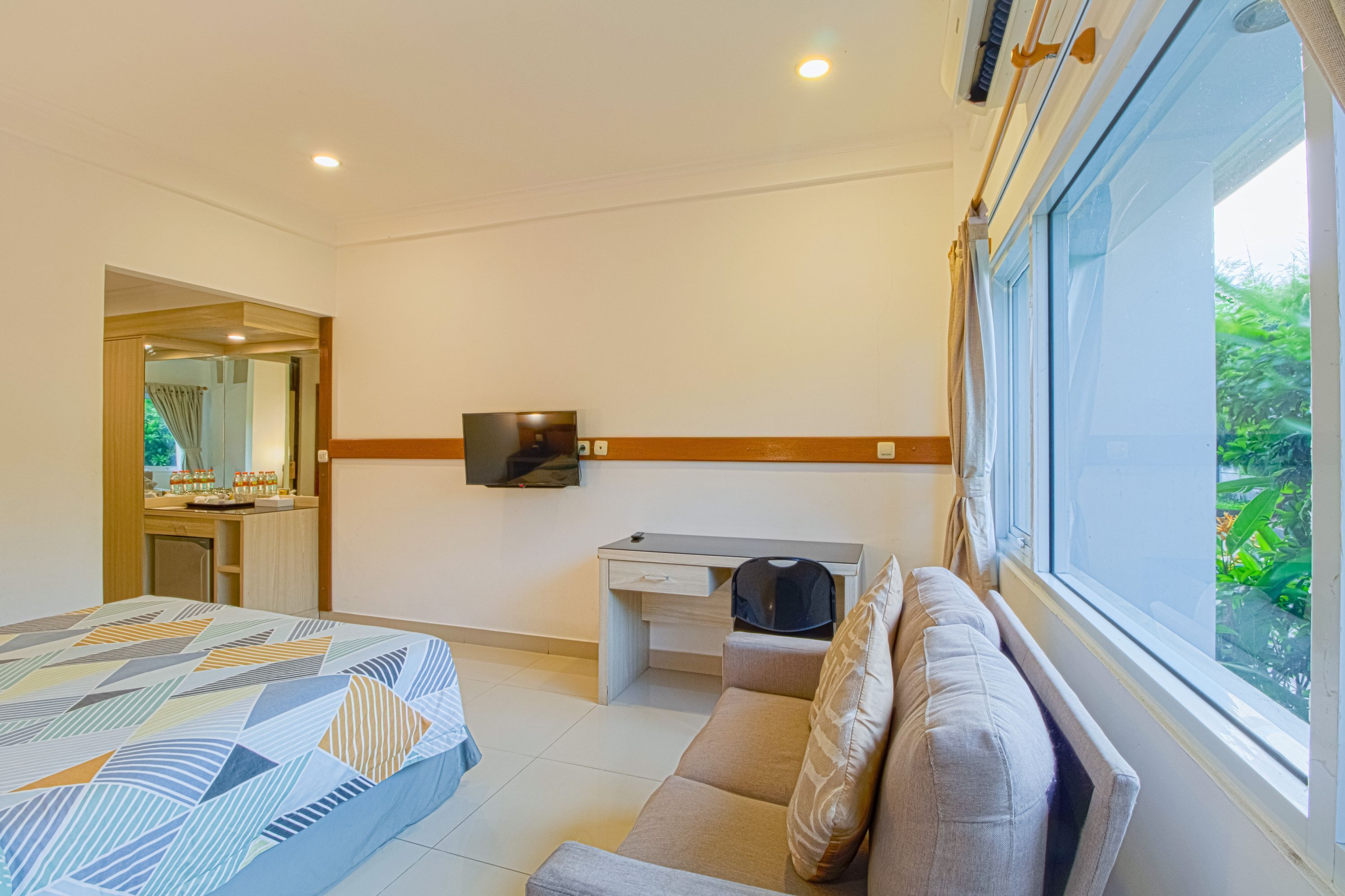 Une chambre d’hôtel équipée d’un lit, d’un bureau, d’un canapé, d’une télévision et d’une fenêtre donnant sur un paysage verdoyant.