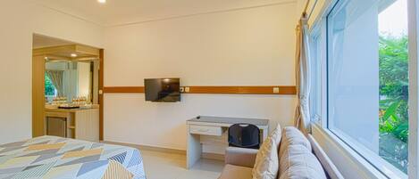 Une chambre d’hôtel équipée d’un lit, d’un bureau, d’un canapé, d’une télévision et d’une fenêtre donnant sur un paysage verdoyant.