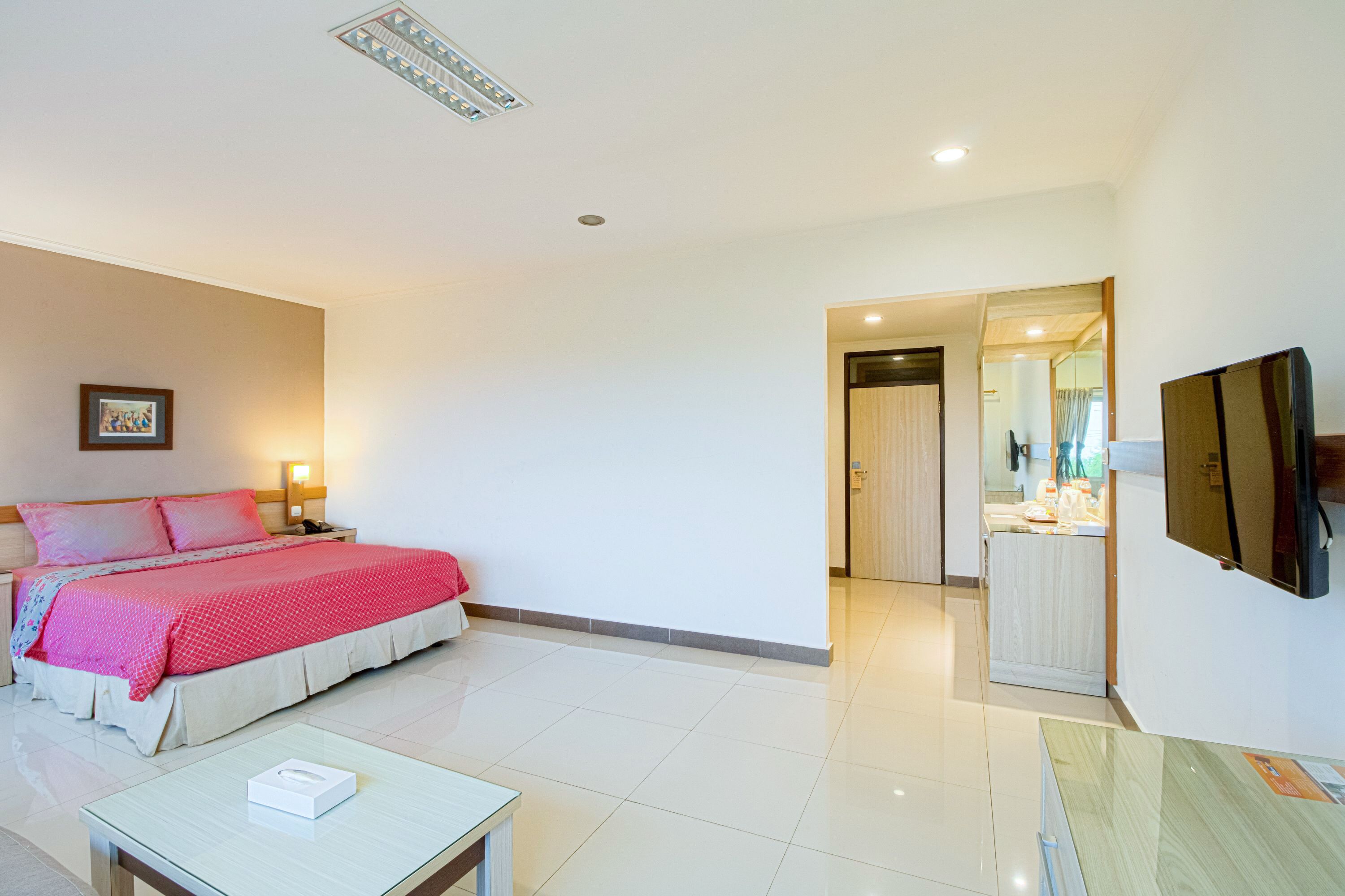 A hotel room with a bed, bedside table, TV, and a bathroom visible through an open door.