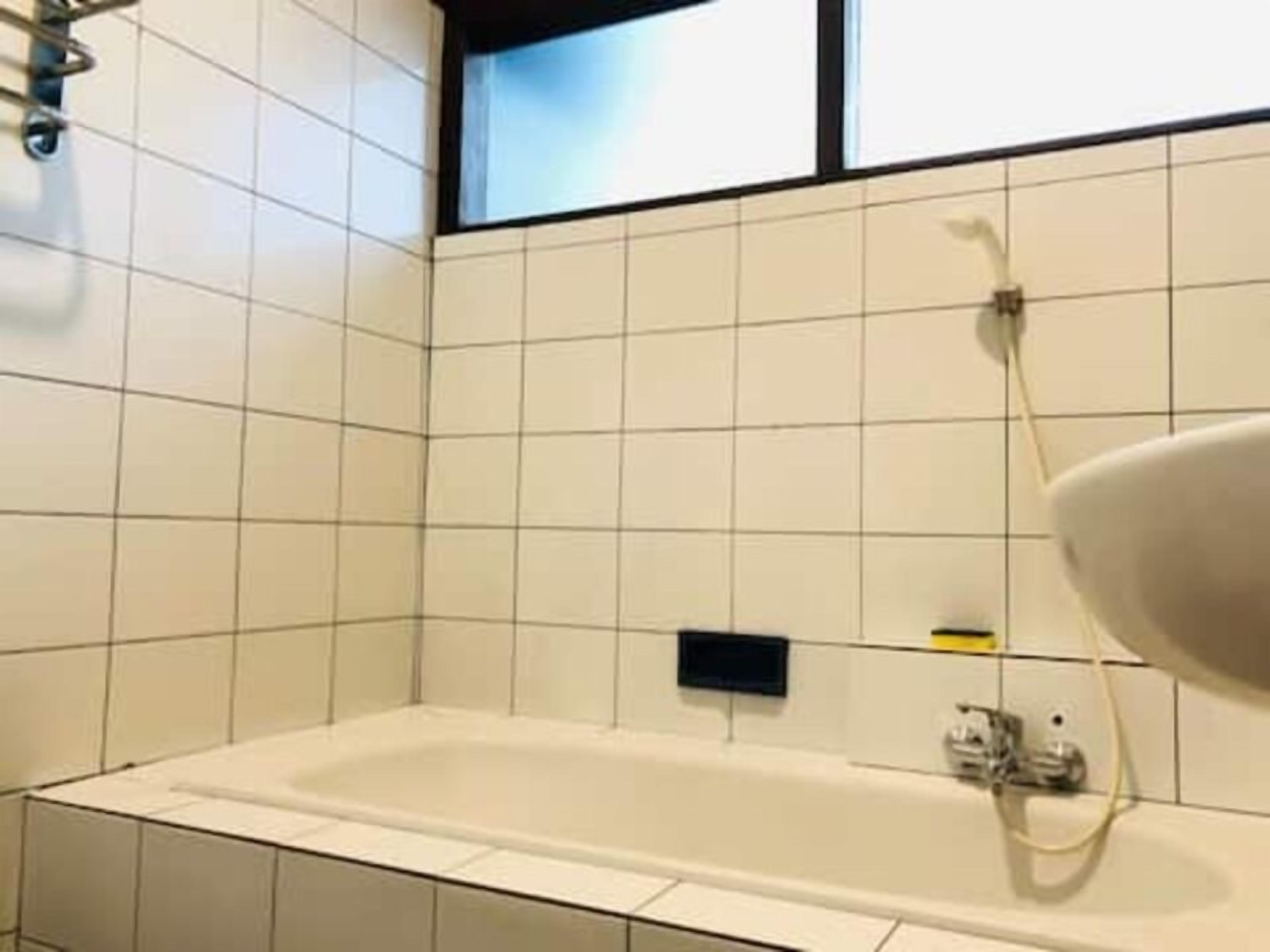 A bathroom with white tiles, a white bathtub, and a window.