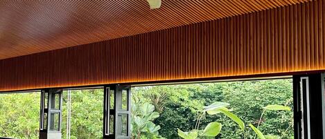 A restaurant with wooden ceiling and tables, chairs, and a view of greenery.
