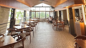 A spacious indoor area with a high ceiling featuring a unique wooden slat design, large windows allowing natural light, and several wooden tables and chairs arranged for dining or seating.