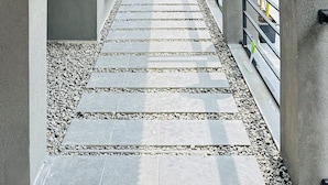 A modern architectural corridor with a wooden ceiling, a glass walkway, and a stone-tiled floor.