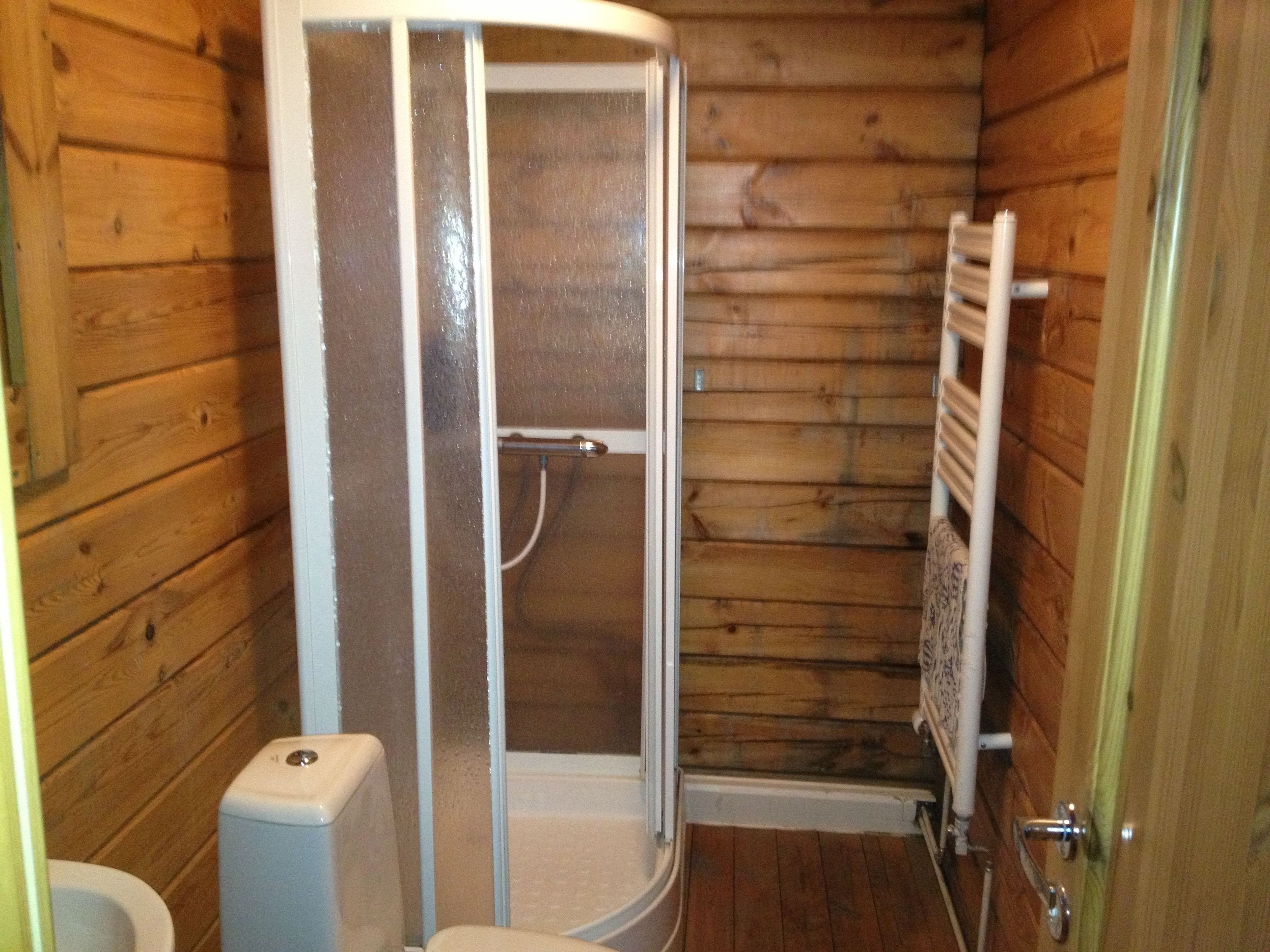 Een badkamer met houten lambrisering, een douchecabine, toilet en handdoekrek.