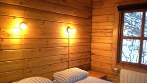 A wooden cabin room with a bed, two bedside lamps, and a window with a view of trees. - North Star Cottage (Rangárþing eystra)