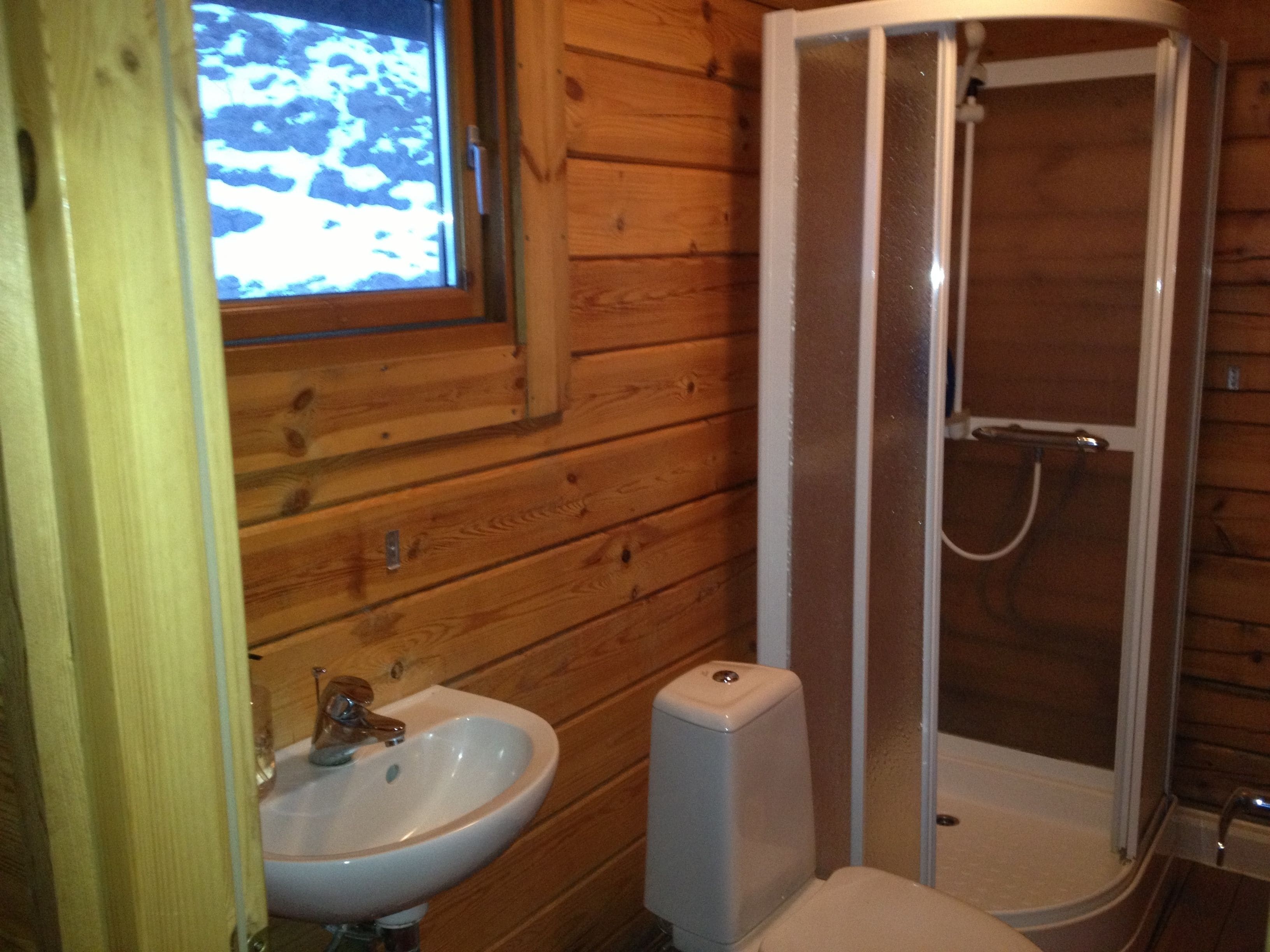 A wooden cabin bathroom with a sink, a shower, and a window.