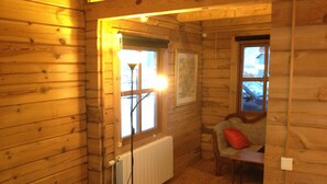 A cozy cabin room with wooden walls, a radiator, a window, and a chair with a red pillow. - North Star Cottage (Rangárþing eystra)