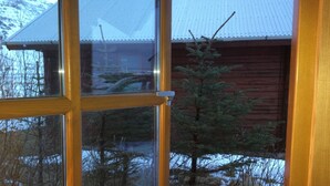 A window with a view of a red building and a coniferous tree. - North Star Cottage (Rangárþing eystra)