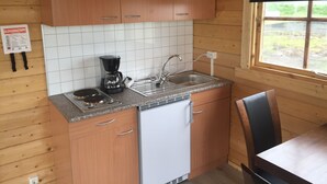 A compact kitchen with wooden cabinets, a coffee maker, a sink, and a small refrigerator. - North Star Cottage (Rangárþing eystra)