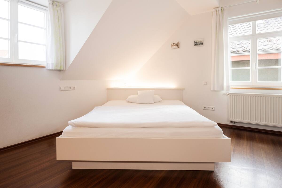 A modern bedroom with a large bed, a sloped ceiling, and a window with curtains.