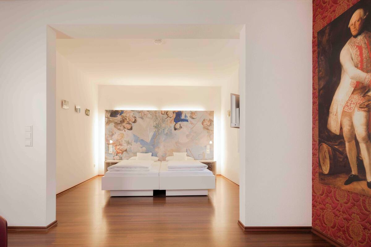 A modern hotel room with a large bed, a mural on the wall, and a painting on the right.