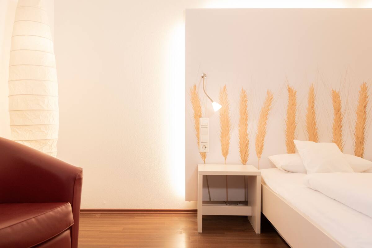 A bedroom with a bed, a nightstand, a lamp, and a wall with decorative elements.