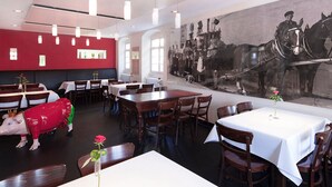 A restaurant with wooden tables and chairs, a red wall with a black and white photo, and a pig statue. - Brauerei Gasthof Krone (Tettnang)