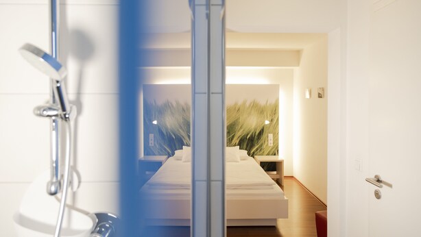 A modern hotel room with a large bed, a shower, and a view of a hallway with a plant. - Brauerei Gasthof Krone (Tettnang)