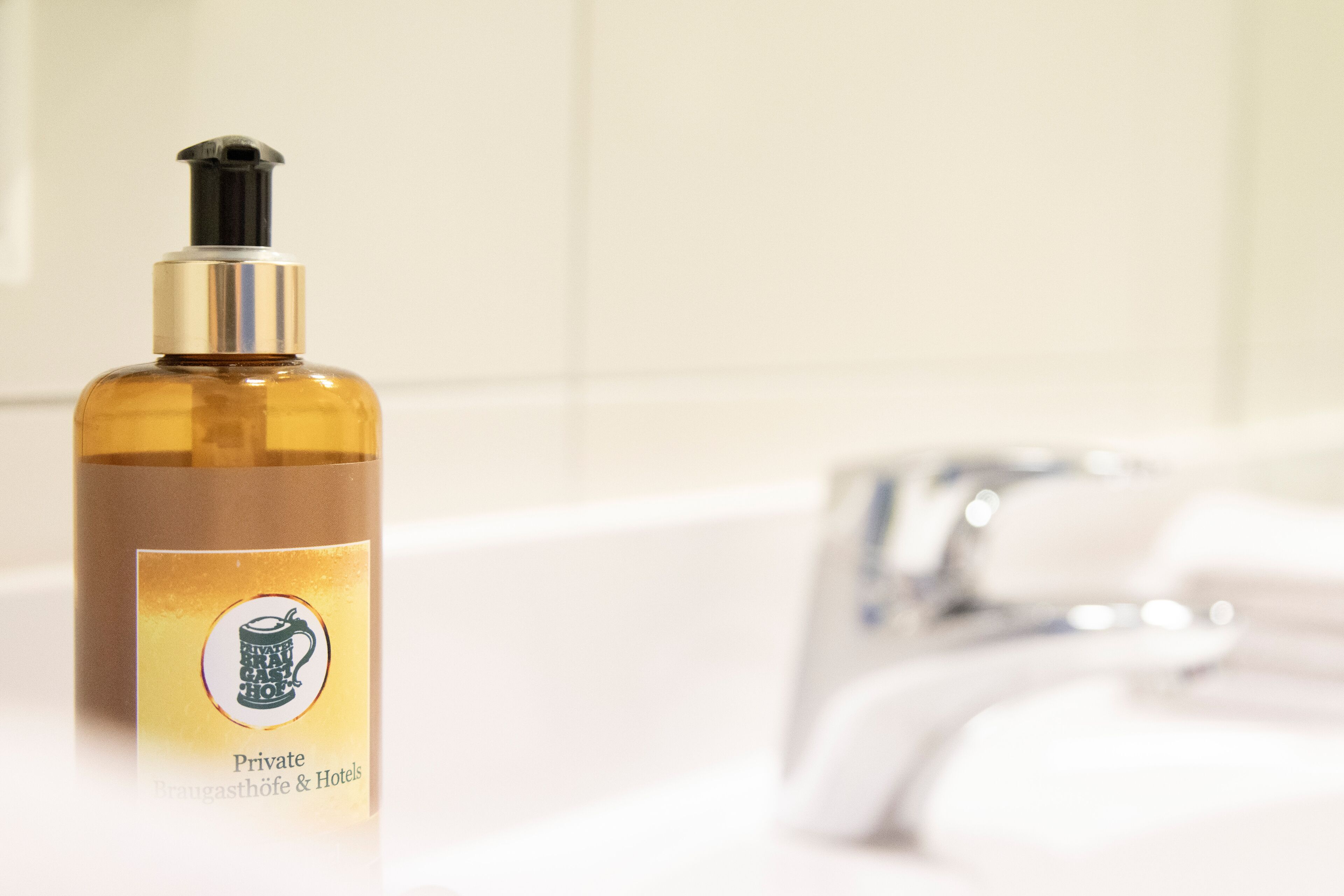 A bottle of Private Brauhaus & Hotels hand soap on a bathroom counter next to a white bathtub with a chrome faucet.