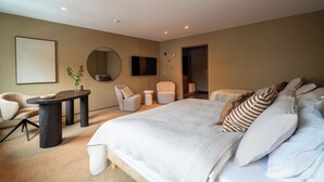 Une chambre moderne avec un grand lit, un miroir rond, deux fauteuils, une petite table et un téléviseur fixé au mur.