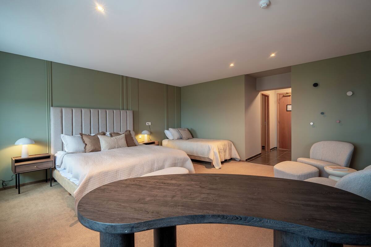 Habitación de hotel con dos camas, una mesa de madera y una silla.