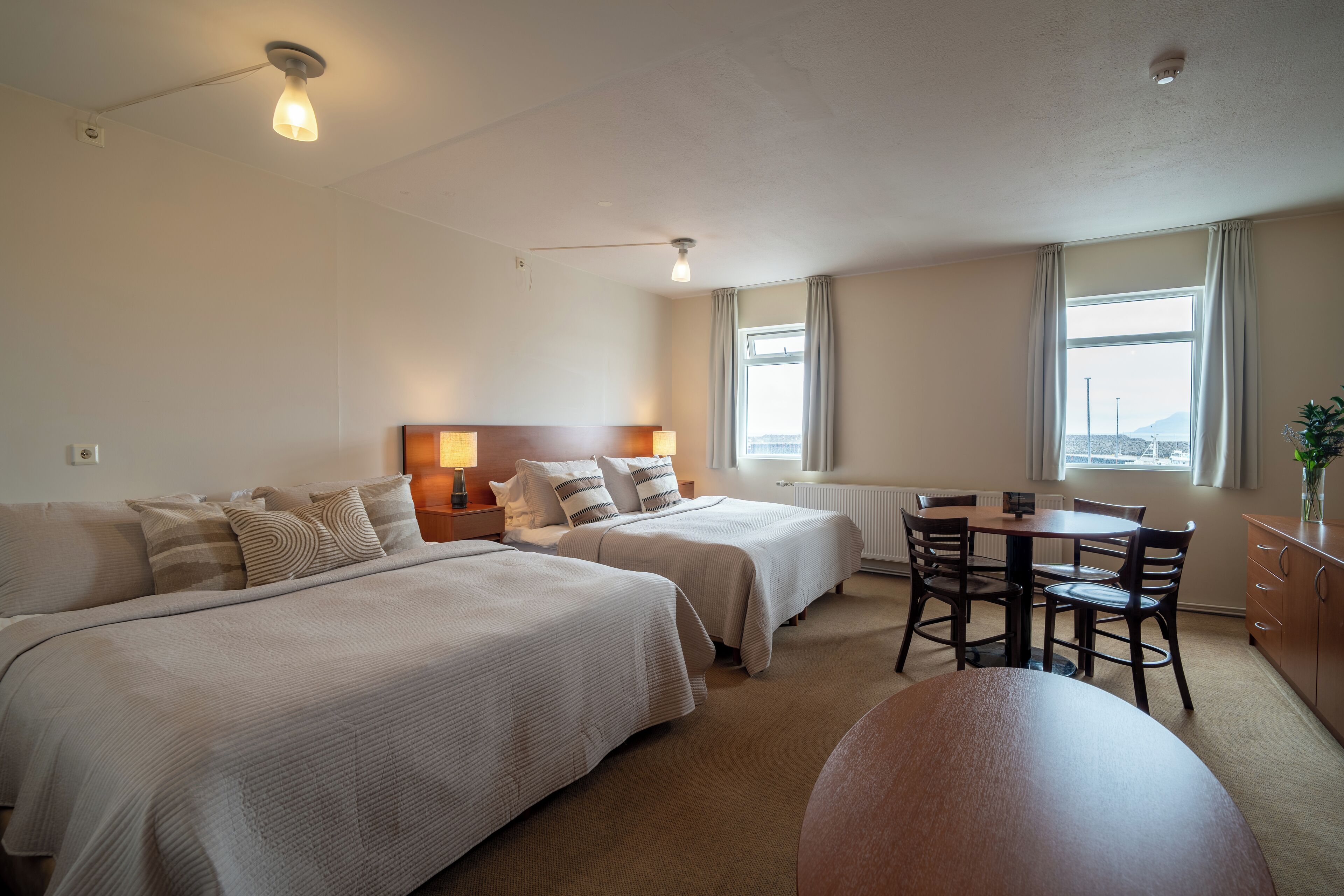 A hotel room with two beds, a dining table, chairs, and a view of the city.