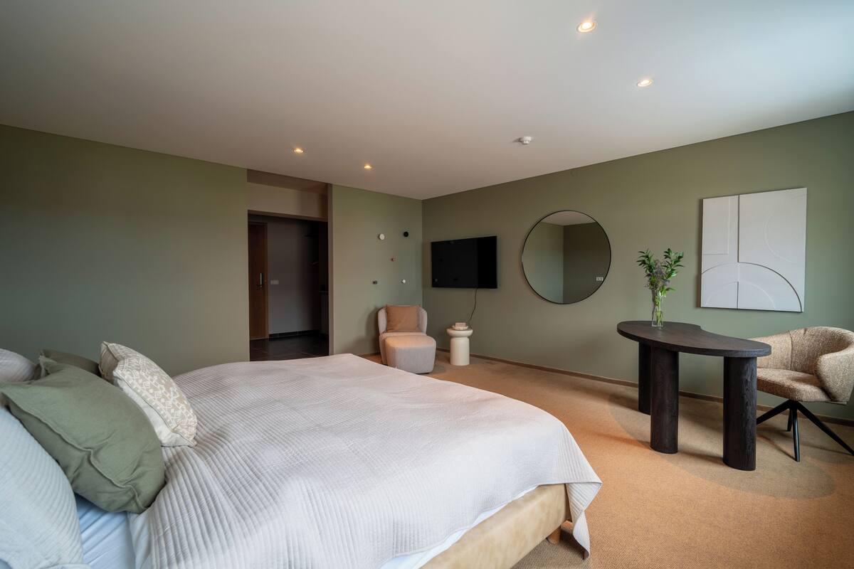 Un dormitorio moderno con una cama grande, una mesa redonda y un televisor montado en la pared.