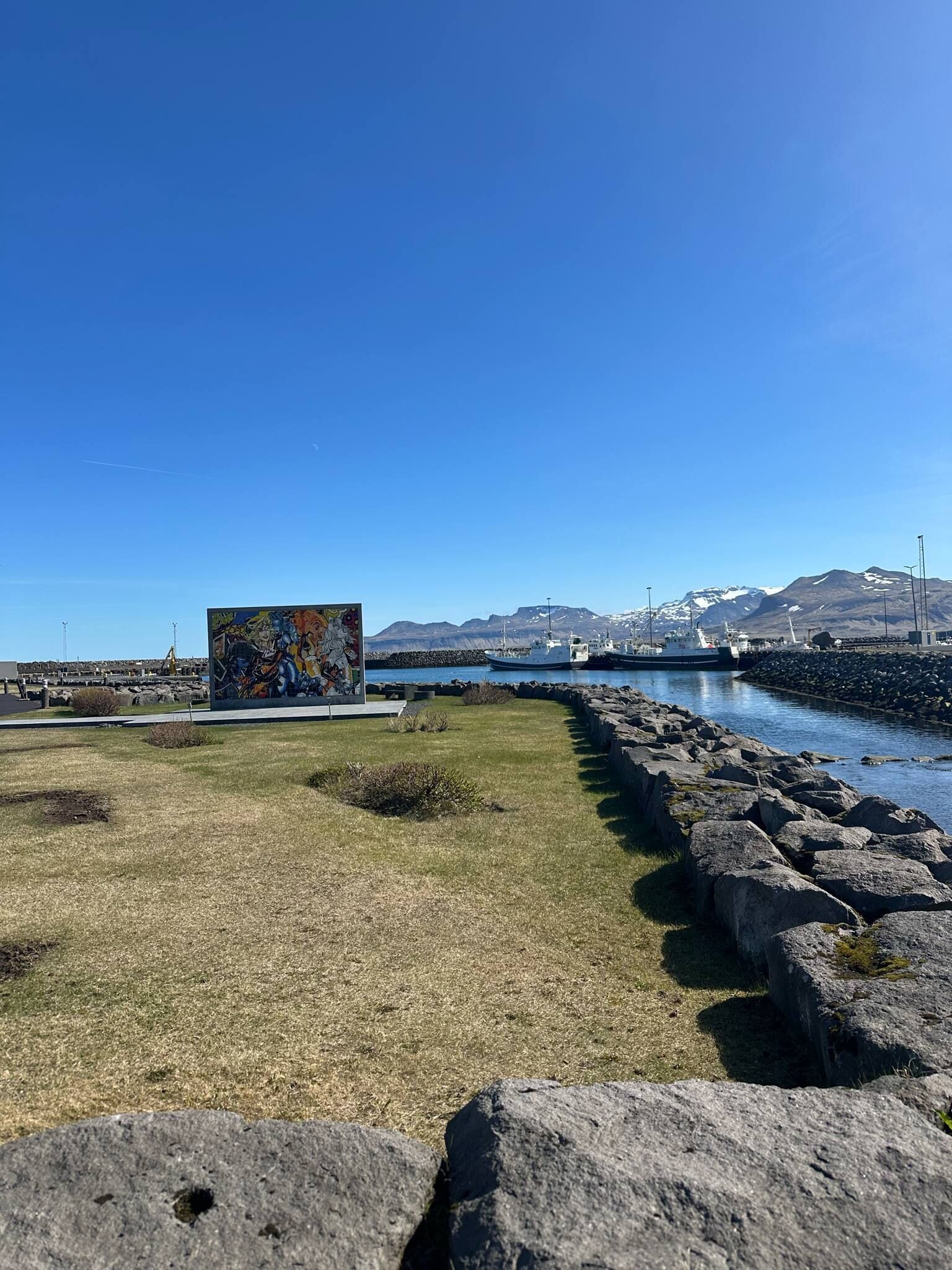 A coastal area with a grassy path, a mural, and a rocky shoreline.