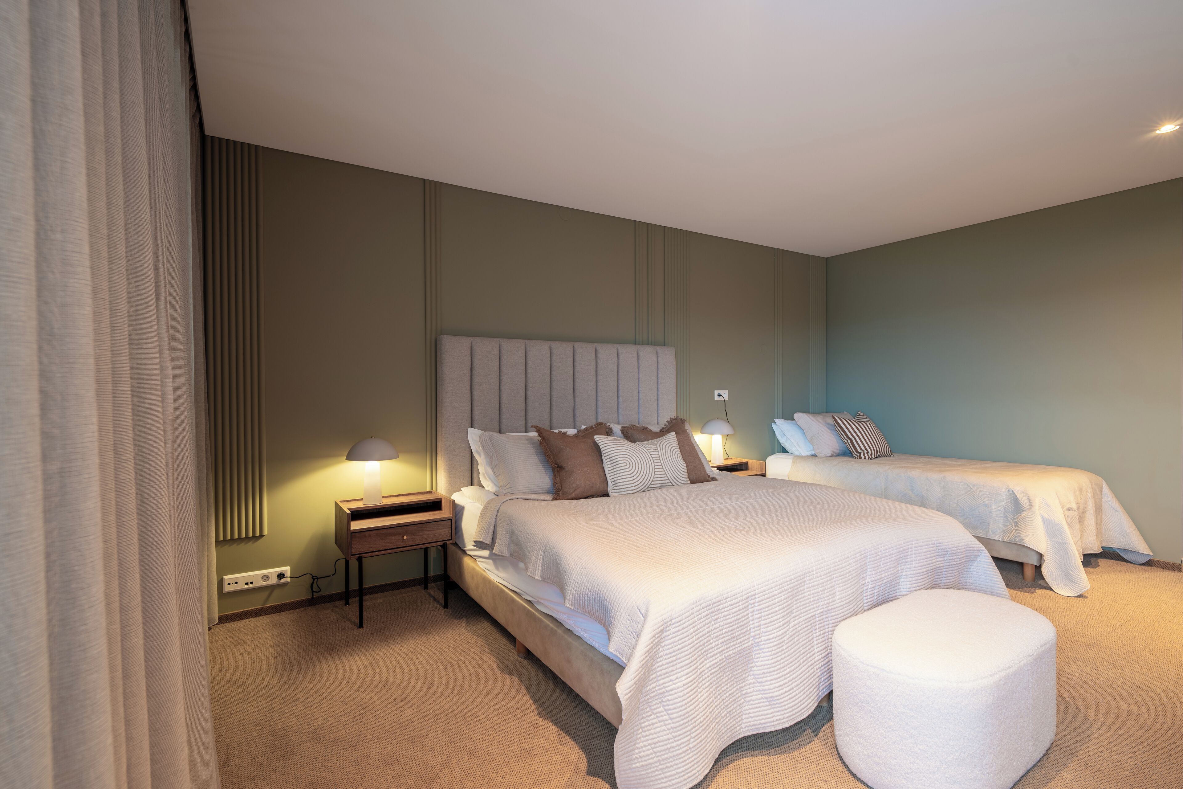 Habitación de hotel con dos camas, una mesita de noche con lámparas, un ventanal con cortinas y suelo alfombrado.