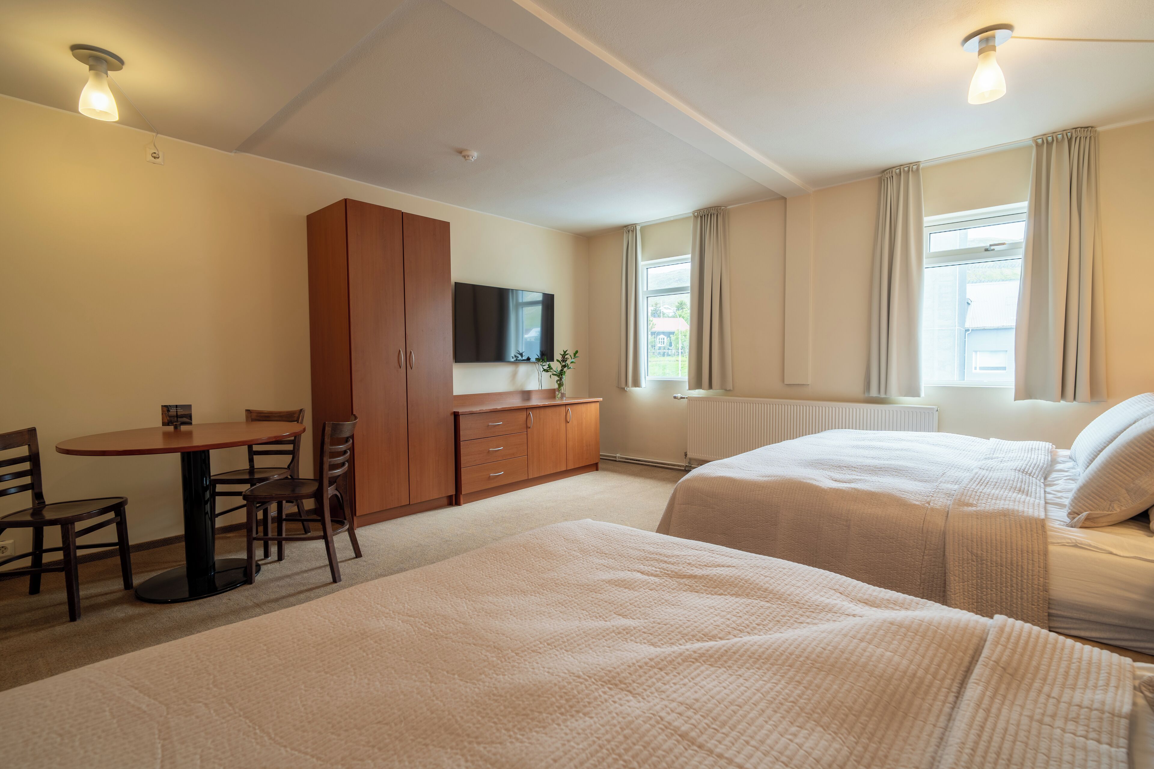Habitación de hotel con dos camas, un escritorio con sillas, un televisor y una ventana con cortinas.