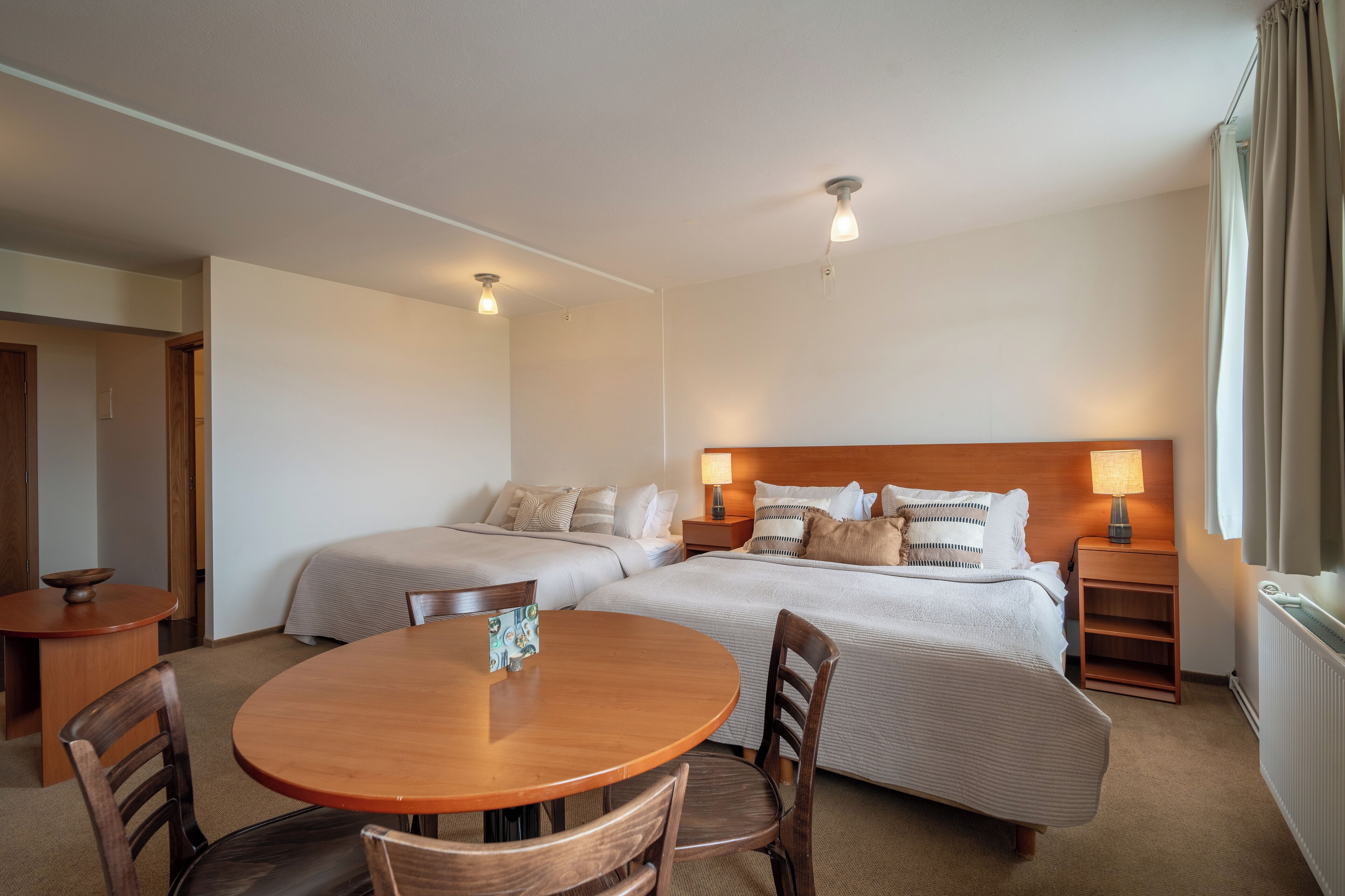 A hotel room with two beds, a wooden dining table, and a small side table.