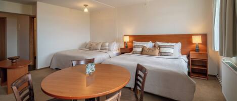 A hotel room with two beds, a wooden dining table, and a small side table.