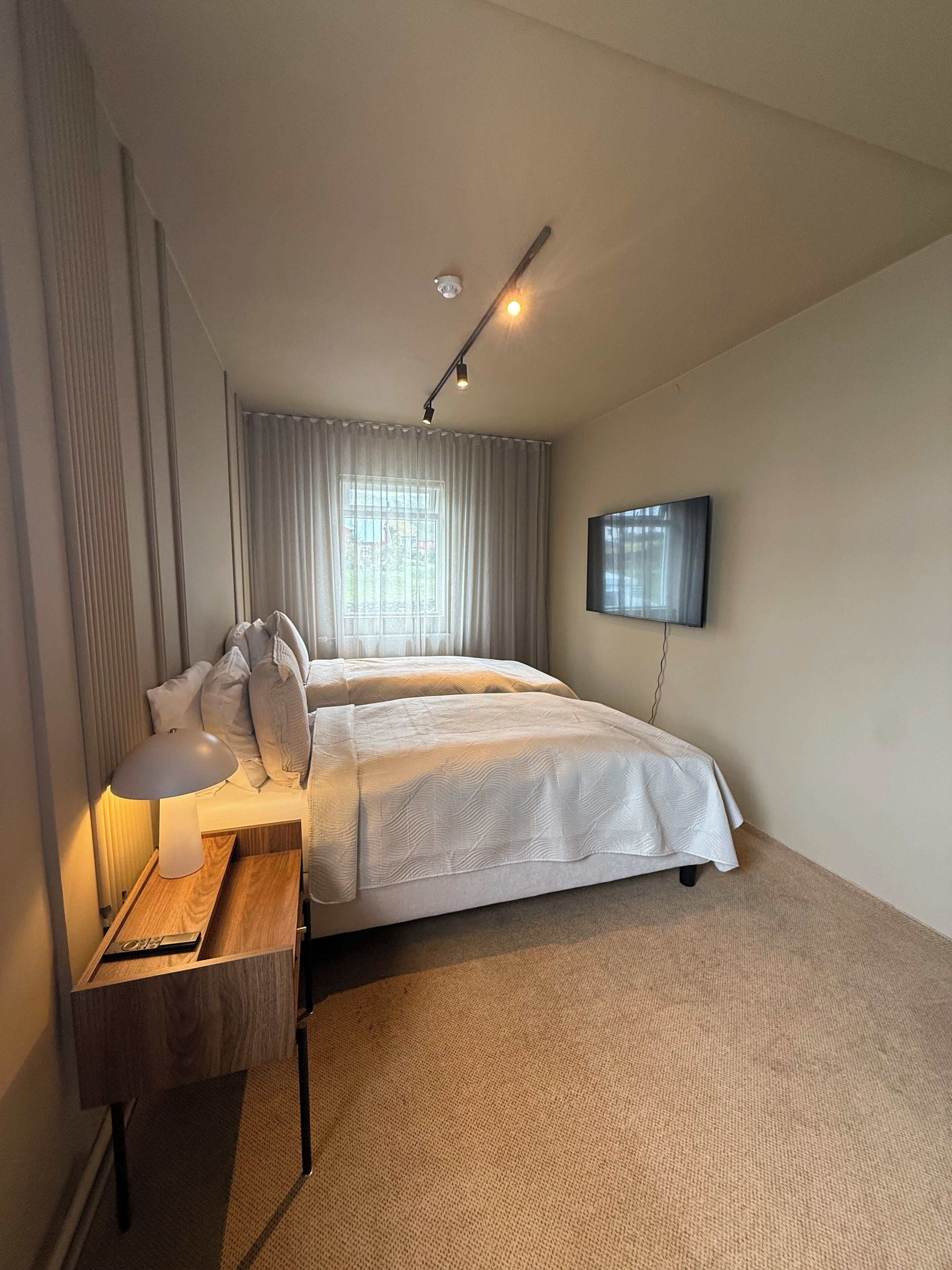 A hotel room with a bed, bedside table, lamp, and a TV mounted on the wall.