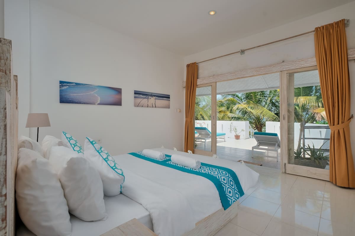 A bedroom with a large bed, a view of the outdoors, and a ceiling fan.