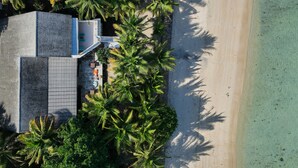 An aerial view of a beachfront property with a modern building, palm trees, and a sandy beach. - MYAMO Beach Lodge (Sumbawa Barat)