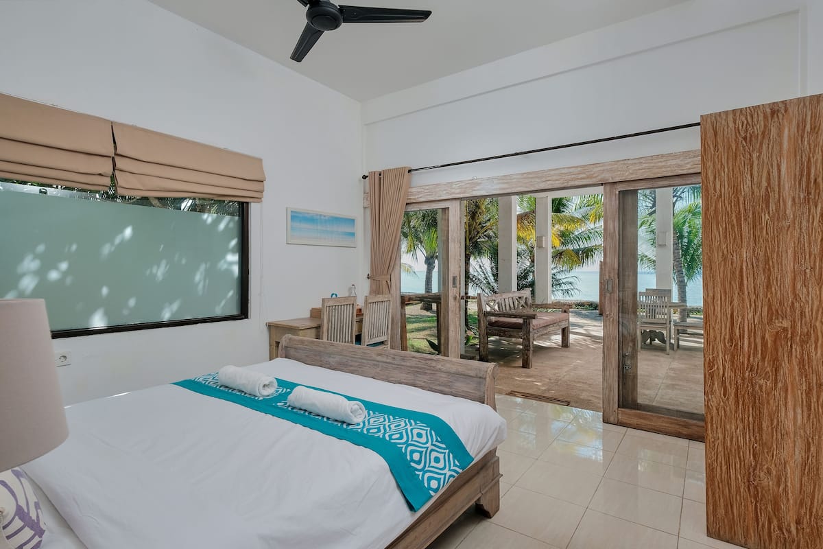 A hotel room with a bed, a ceiling fan, a large window, and a view of the outdoors.