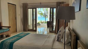 A hotel room with a bed, a bench, a lamp, and a view of the beach and ocean through an open door. - MYAMO Beach Lodge (Sumbawa Barat)