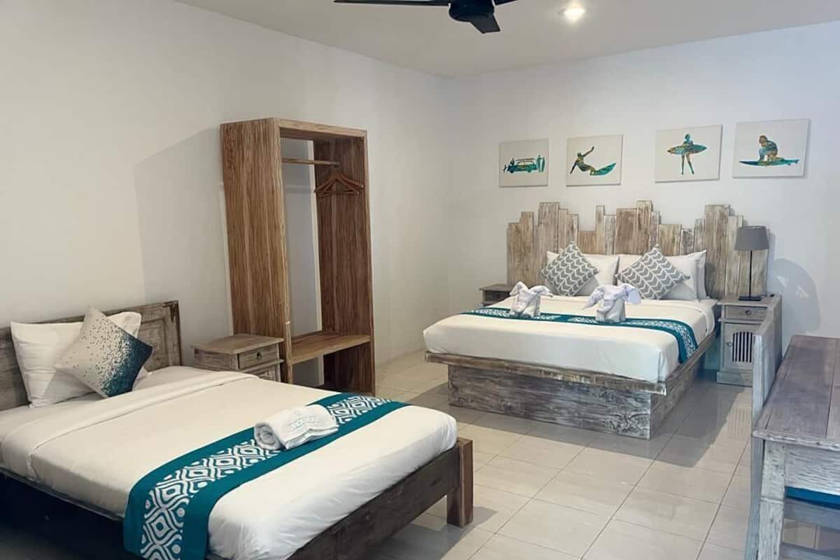 A hotel room with two beds, a wooden wardrobe, a desk, and artwork on the wall.