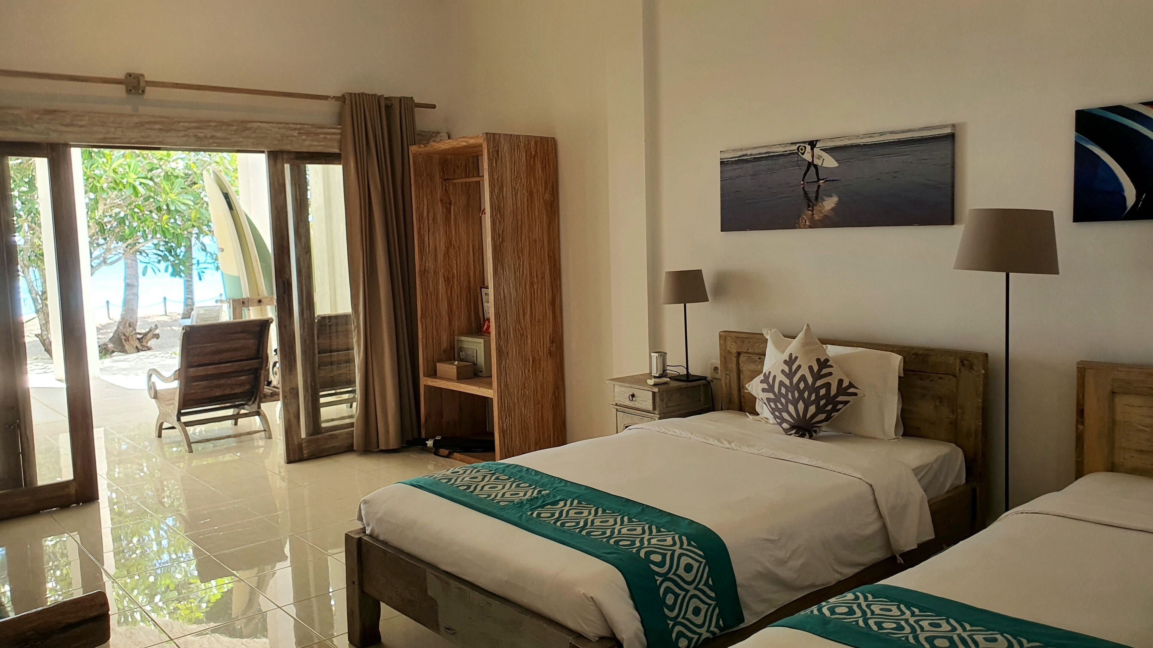 Habitación de hotel con cama, mesita de noche, lámpara, silla, armario de madera y vista a la playa.