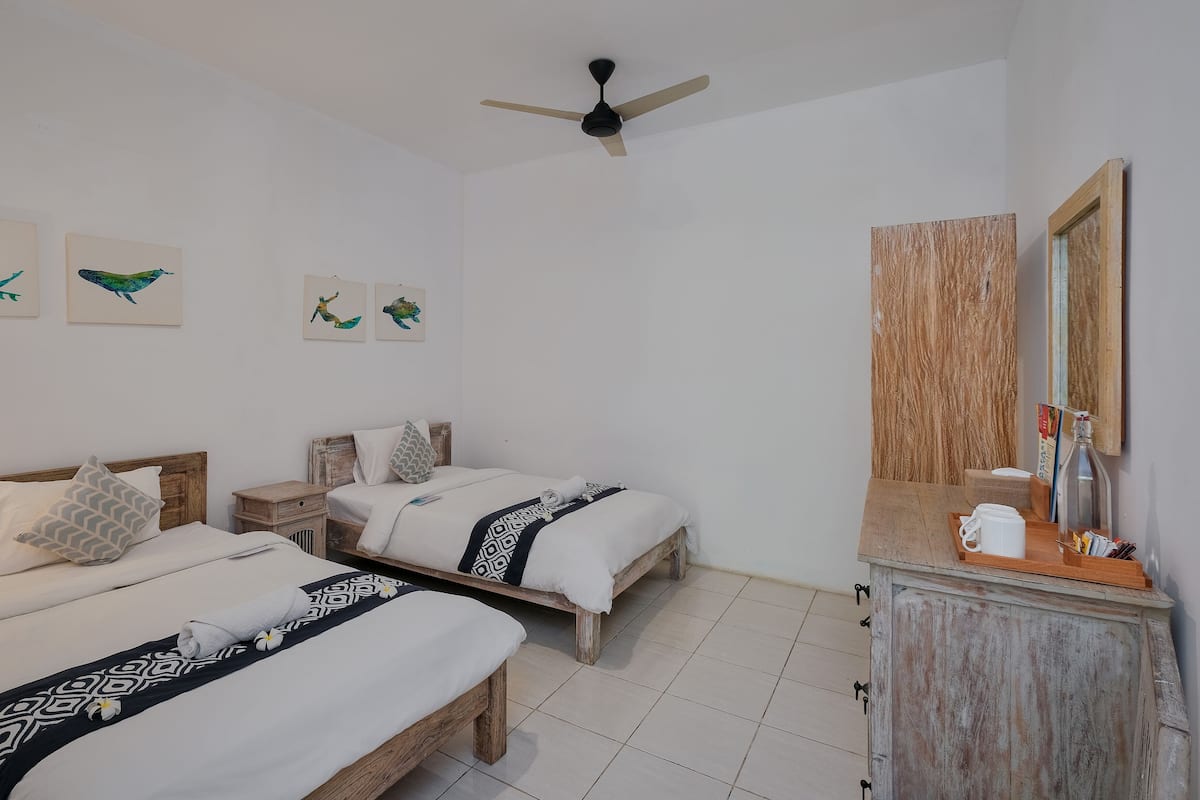 A hotel room with two beds, a wooden nightstand, a dresser, and a ceiling fan.