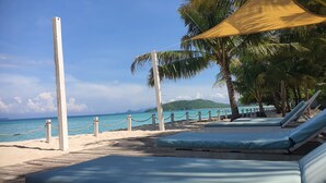 A beachside lounge area with sun loungers, a wooden deck, and a view of the ocean. - MYAMO Beach Lodge (Sumbawa Barat)