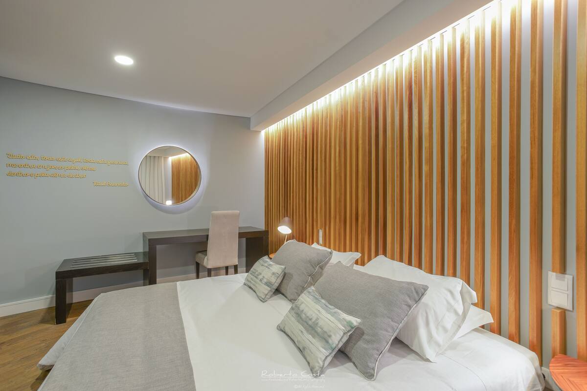 A modern bedroom with a bed, bedside tables, a chair, a round mirror, and a wall with vertical wooden slats.