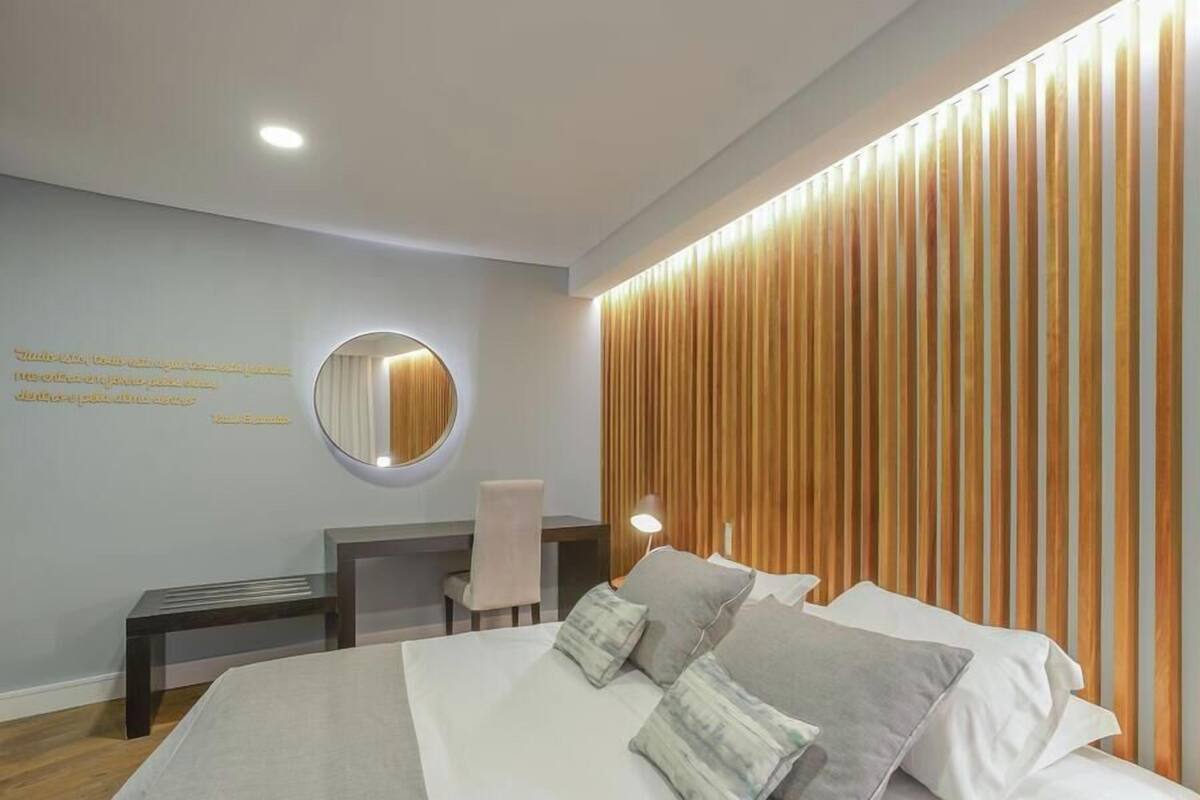 A hotel room with a bed, bedside table, chair, and a wall-mounted mirror.