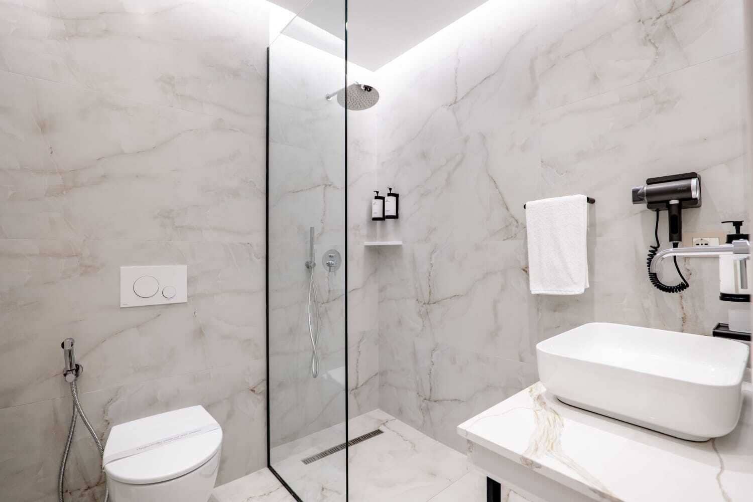 Un baño moderno con ducha envuelta en vidrio, inodoro blanco y un lavamanos amplio con espejo.