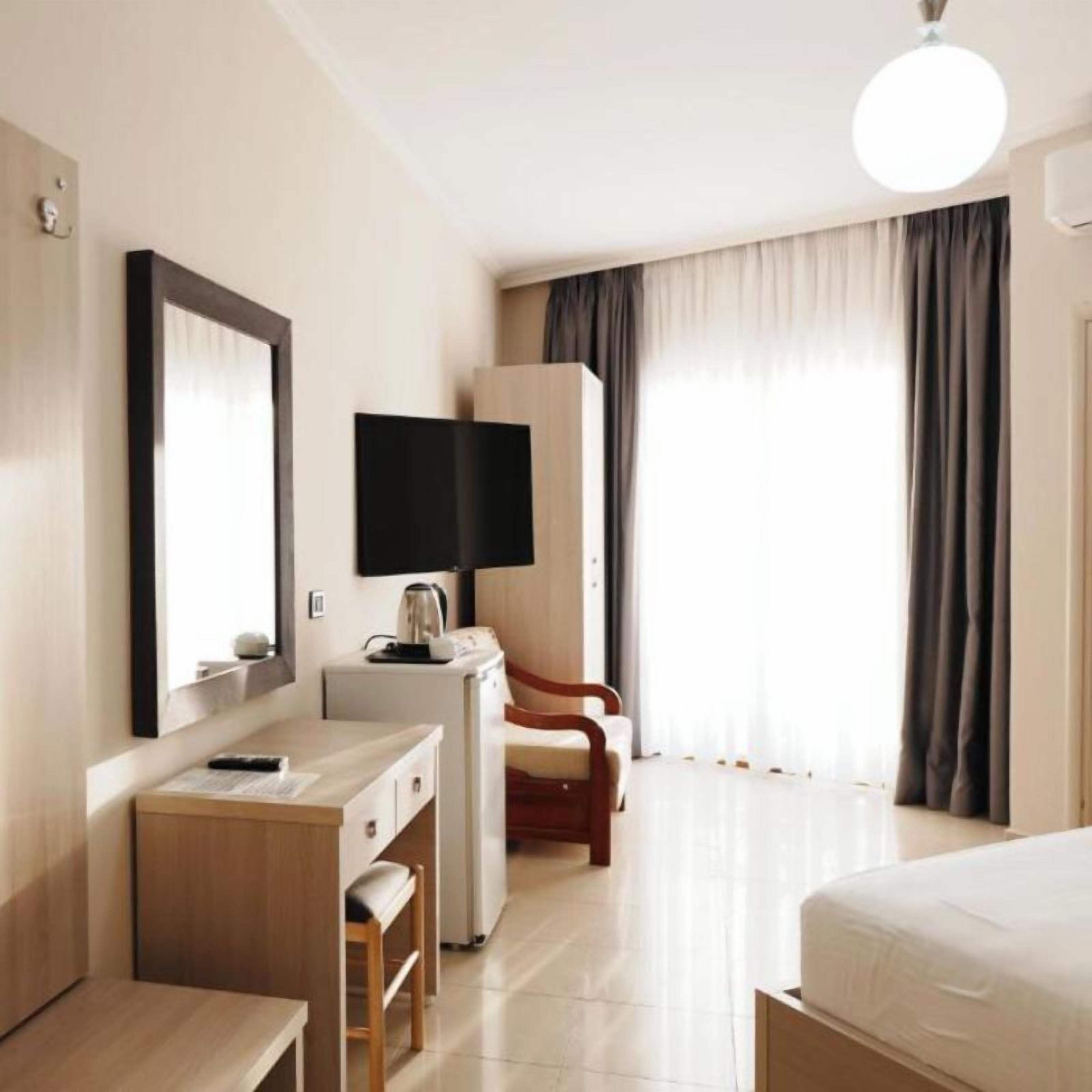 A hotel room with a bed, a desk with a chair, a television, and a wardrobe.
