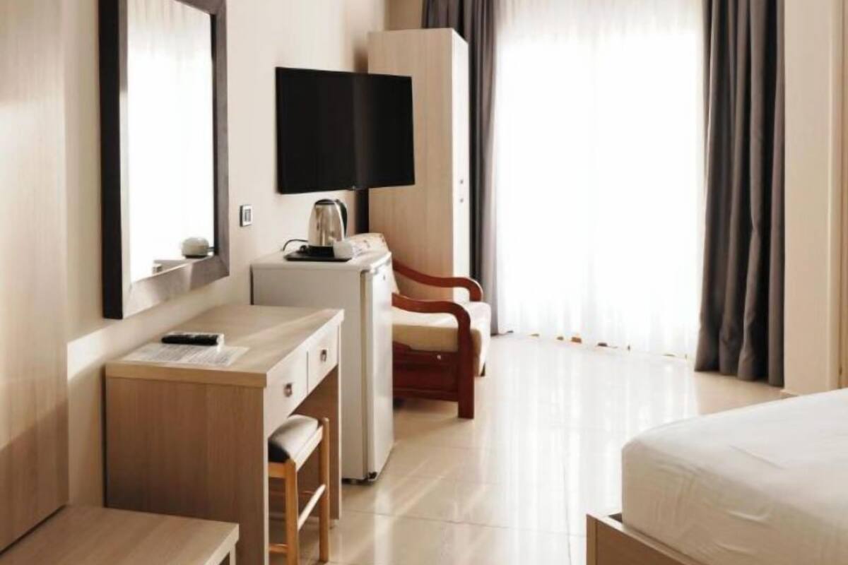 A hotel room with a bed, a desk with a chair, a television, and a wardrobe.
