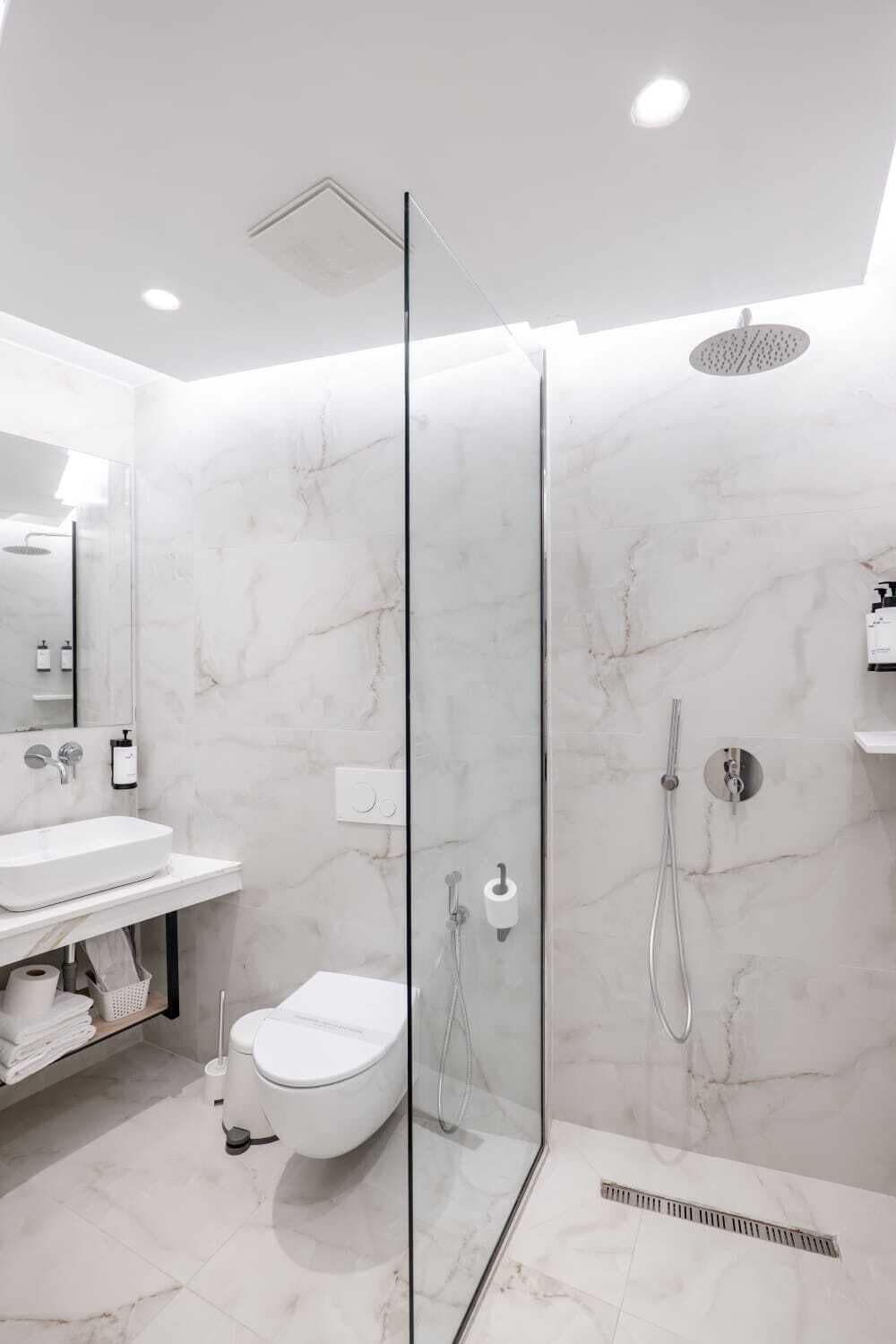Un baño moderno con cabina de ducha de vidrio, inodoro blanco y pared con azulejos de mármol.