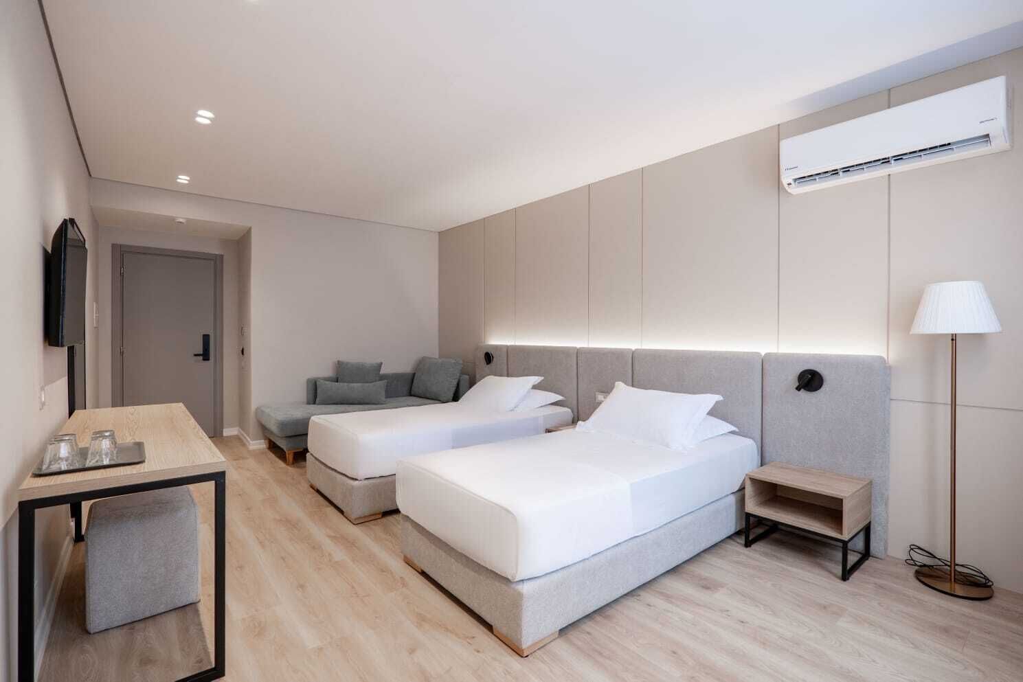 A modern hotel room with two beds, a desk, a TV, and an air conditioning unit.