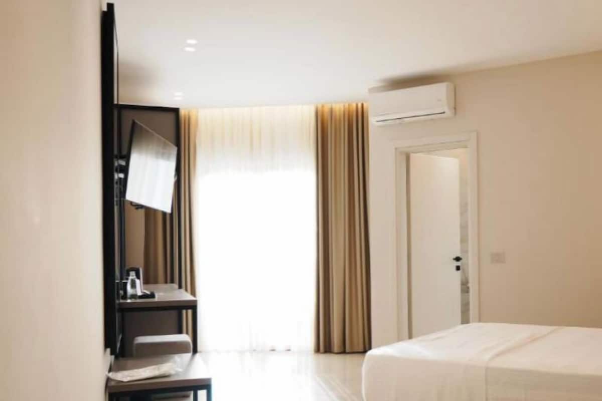 Una habitación de hotel con una cama, un escritorio con una silla, un espejo y un equipo de aire acondicionado.