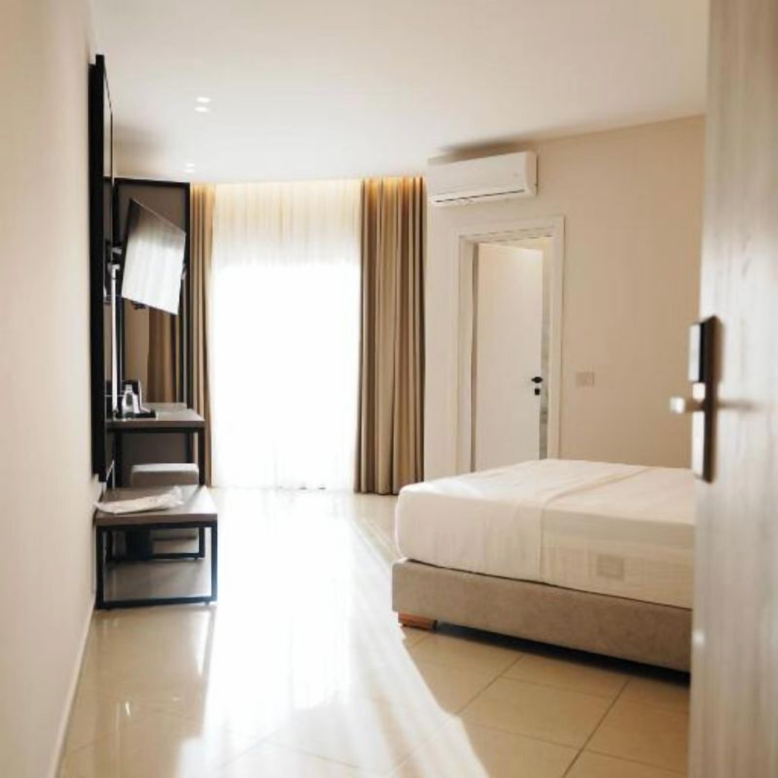 A hotel room with a bed, a desk, a chair, a mirror, and an air conditioning unit.