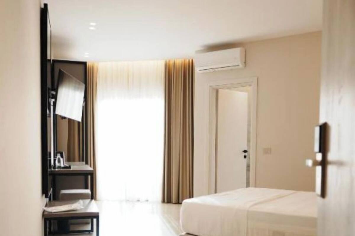A hotel room with a bed, a desk, a chair, a mirror, and an air conditioning unit.