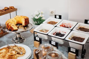 Buffet com diversas opções de comida, incluindo panquecas, um bolo e vários molhos.