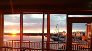 Una terraza de madera con mesa y sillas, con vistas a un puerto deportivo con barcos y una montaña al fondo.